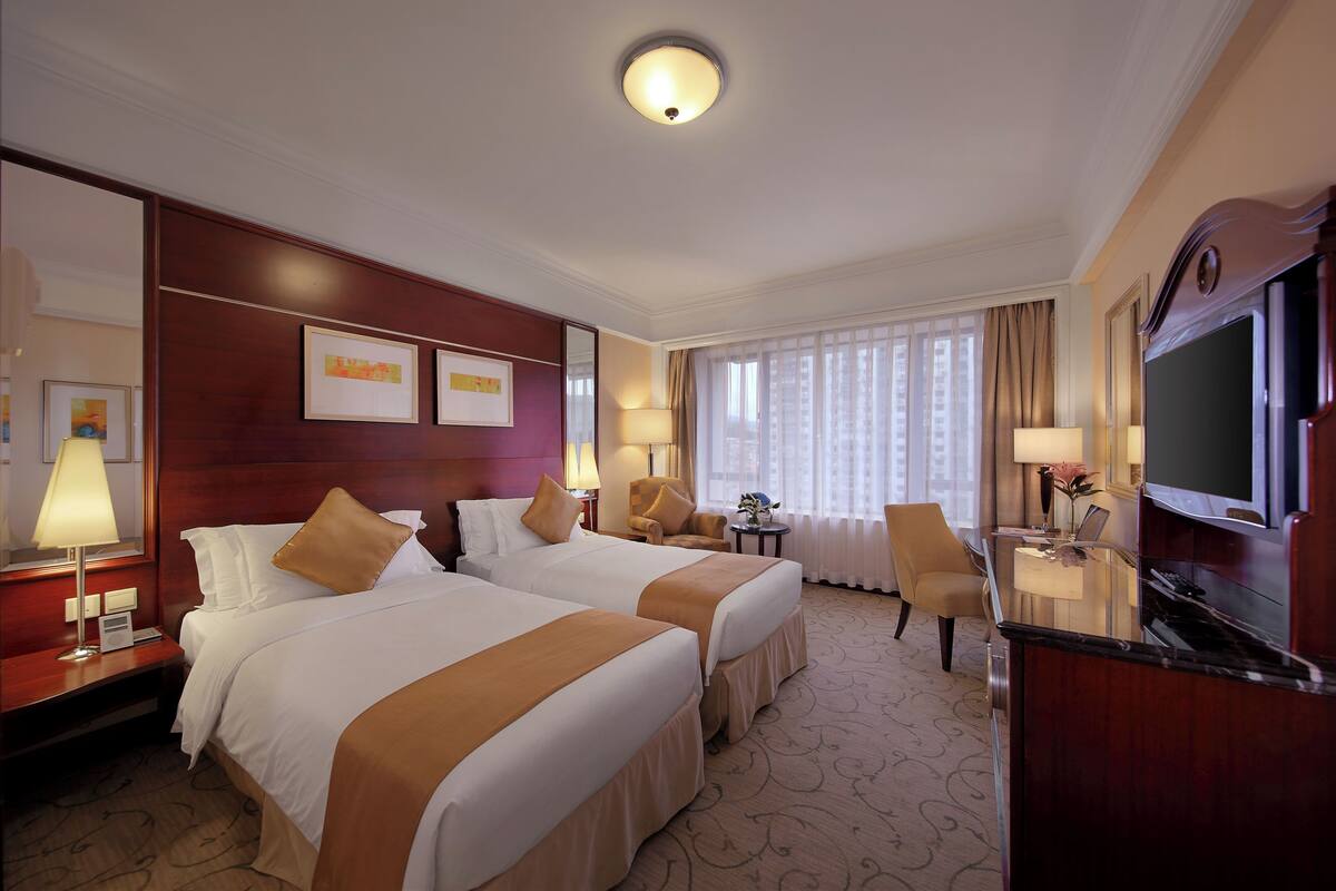 A hotel room with two beds, a TV, a desk, and a chair.