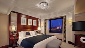 A hotel room with a large bed, a television, a nightstand, and a view of a cityscape at dusk. - Hotel Royal Macau (Macau)