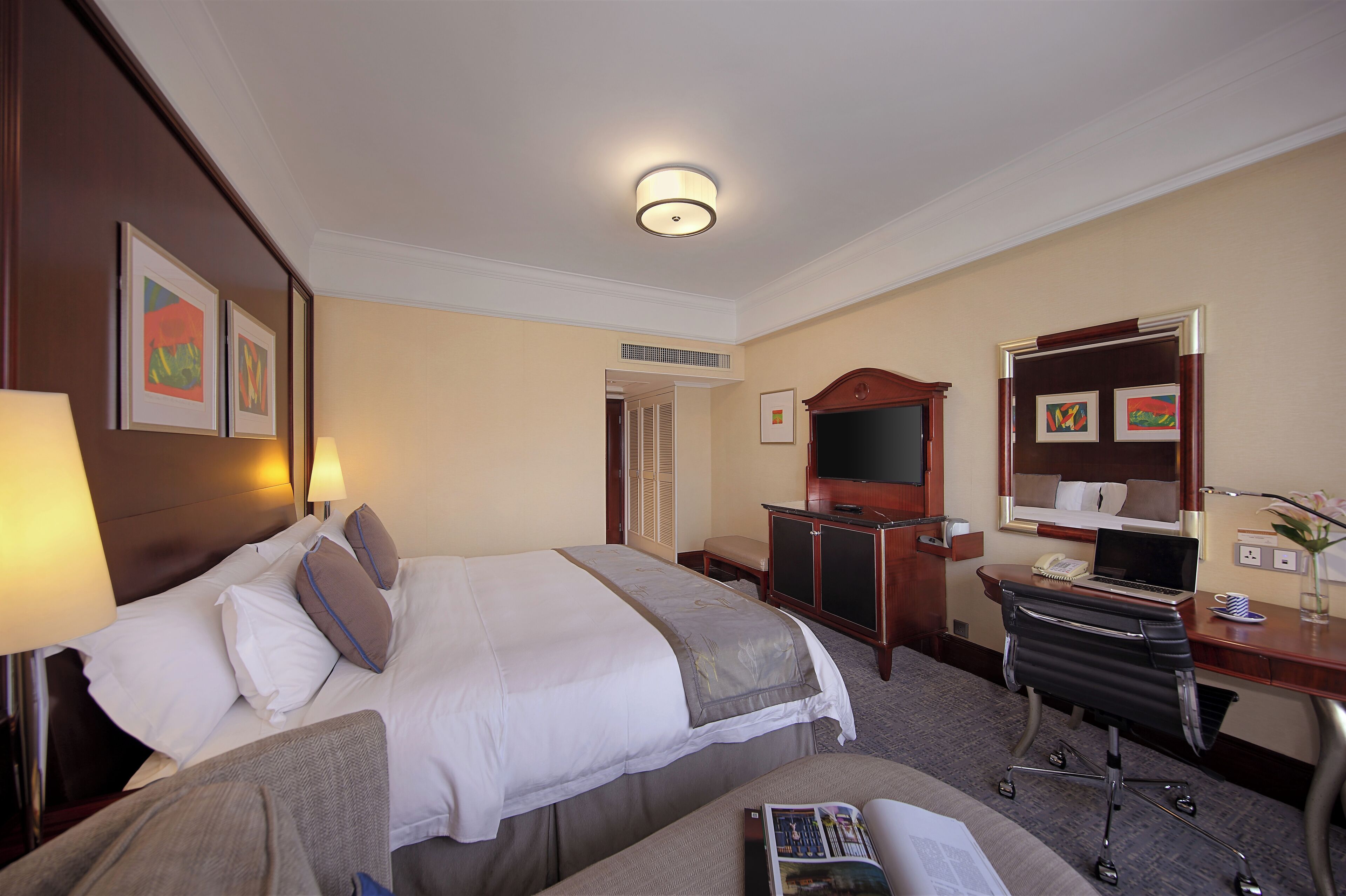 A hotel room with two beds, a desk with a computer, a chair, a TV, and artwork on the walls.