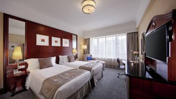 A hotel room with two beds, a TV, a desk, and a large window.