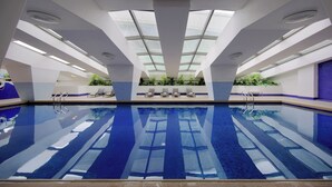 An indoor swimming pool with clear blue water, a glass ceiling, and lounge chairs along the sides. - Hotel Royal Macau (Macau)