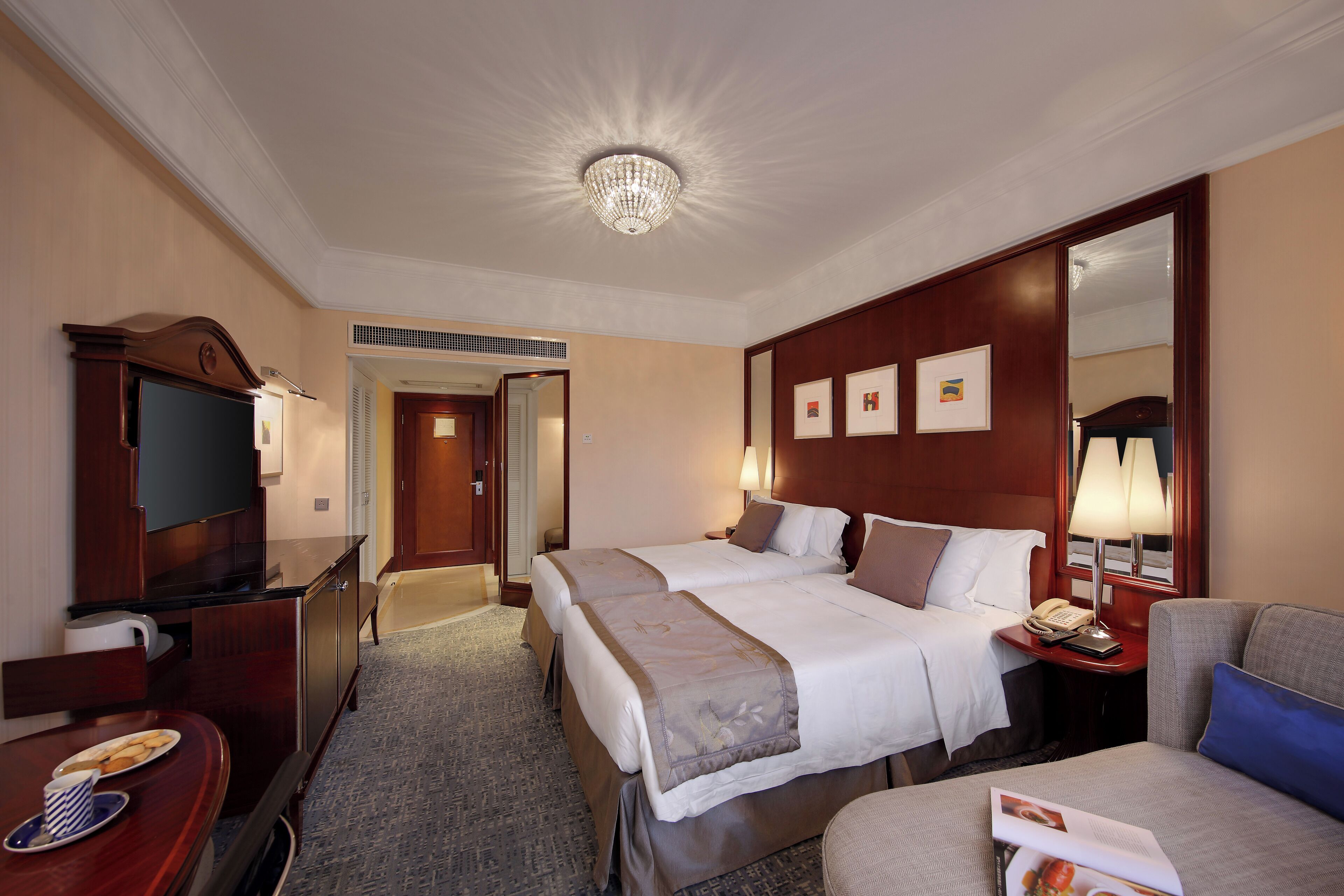 Habitación de hotel con dos camas, un televisor, un escritorio con cafetera y un espejo.