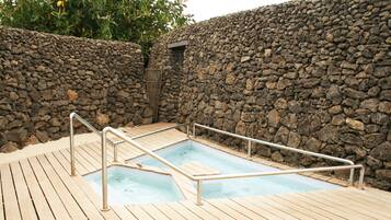 Eine Holzterrasse mit einem rechteckigen Whirlpool, umgeben von einer Steinmauer.