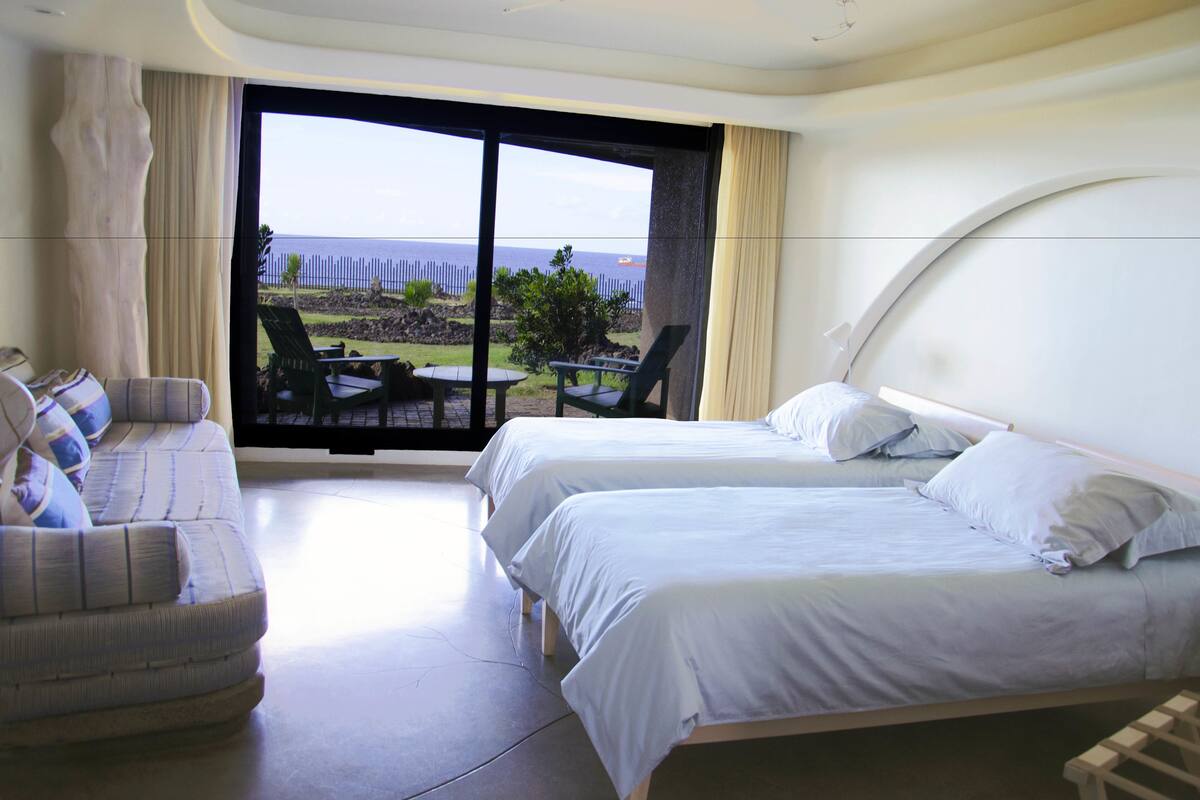 A hotel room with two beds, a sofa, and a balcony with a view of the sea.
