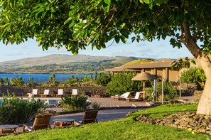 A poolside area with lounge chairs, a small pool, and a view of the ocean and hills.