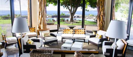 A modern lounge area with a view of the ocean, featuring a sofa set, two lamps, and a coffee table.