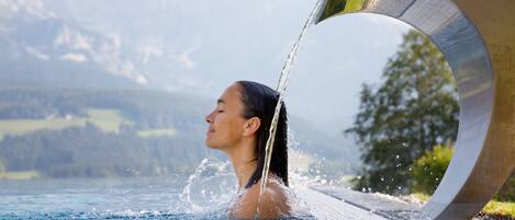 A person in a swimming pool with water flowing from a structure.
