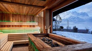Eine Holzsauna mit Bänken und einem Steingefäß mit Blick auf eine verschneite Berglandschaft.