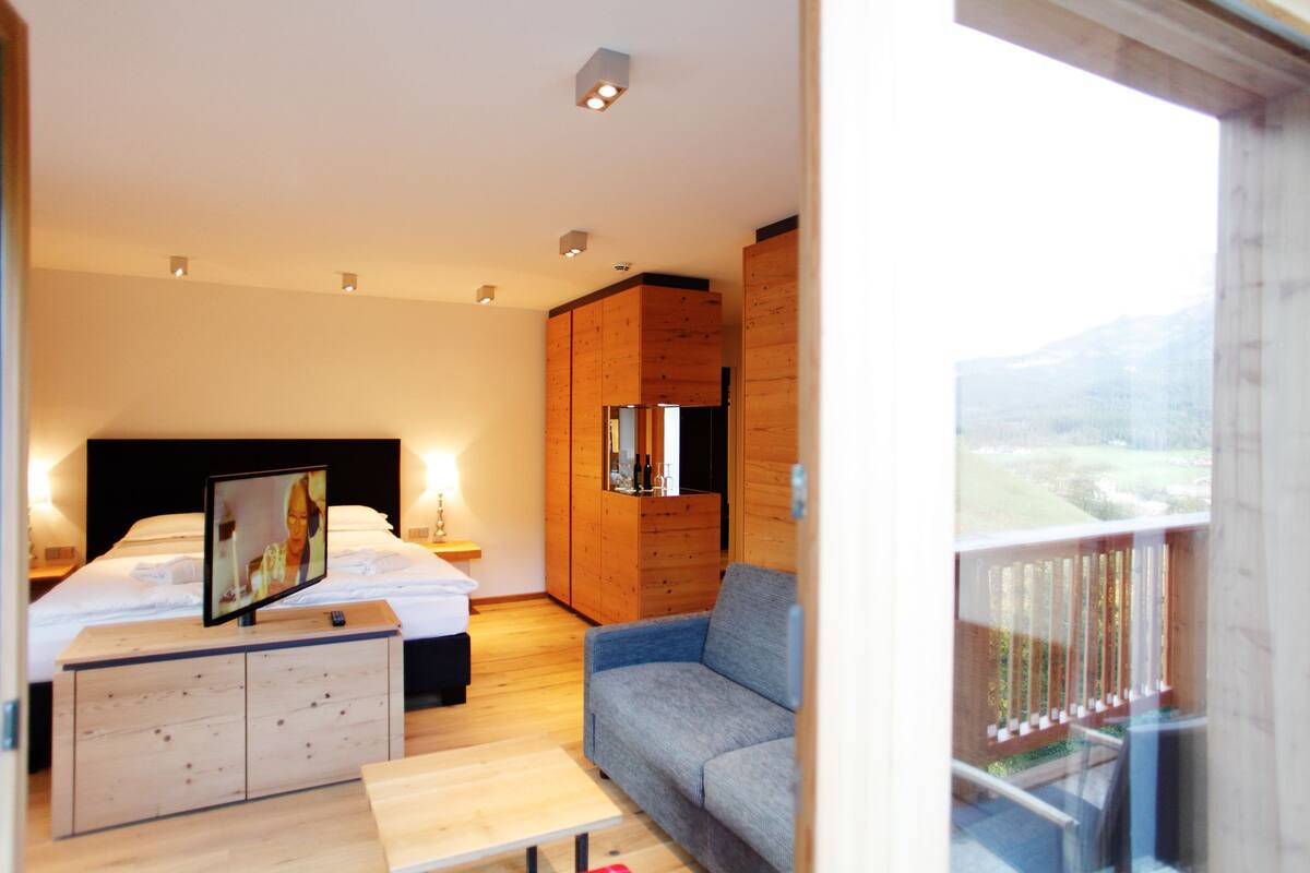 Une chambre d’hôtel moderne équipée d’un lit, d’un bureau, d’un canapé et d’un balcon offrant une vue sur les montagnes.