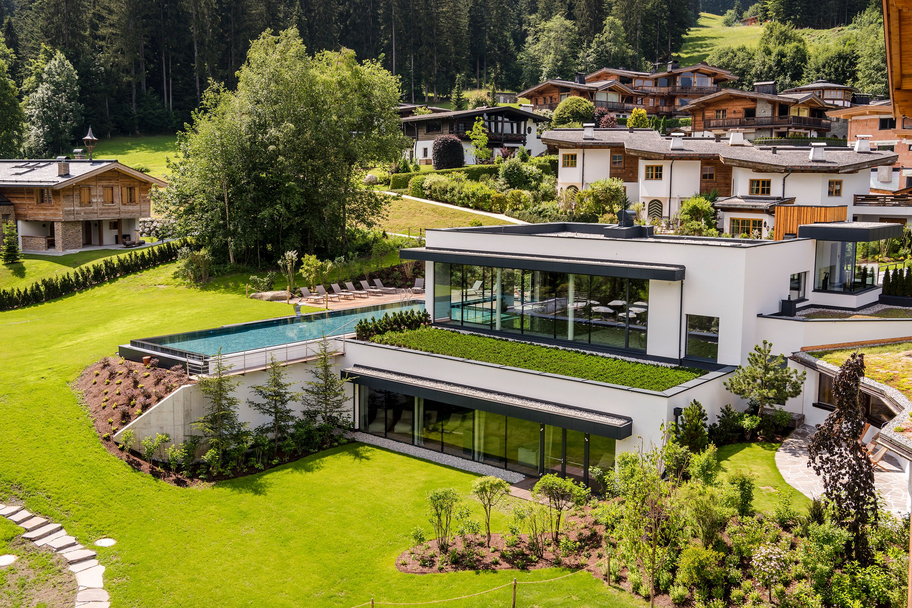 Una casa moderna con un amplio ventanal de vidrio, piscina y un jardín cuidado.