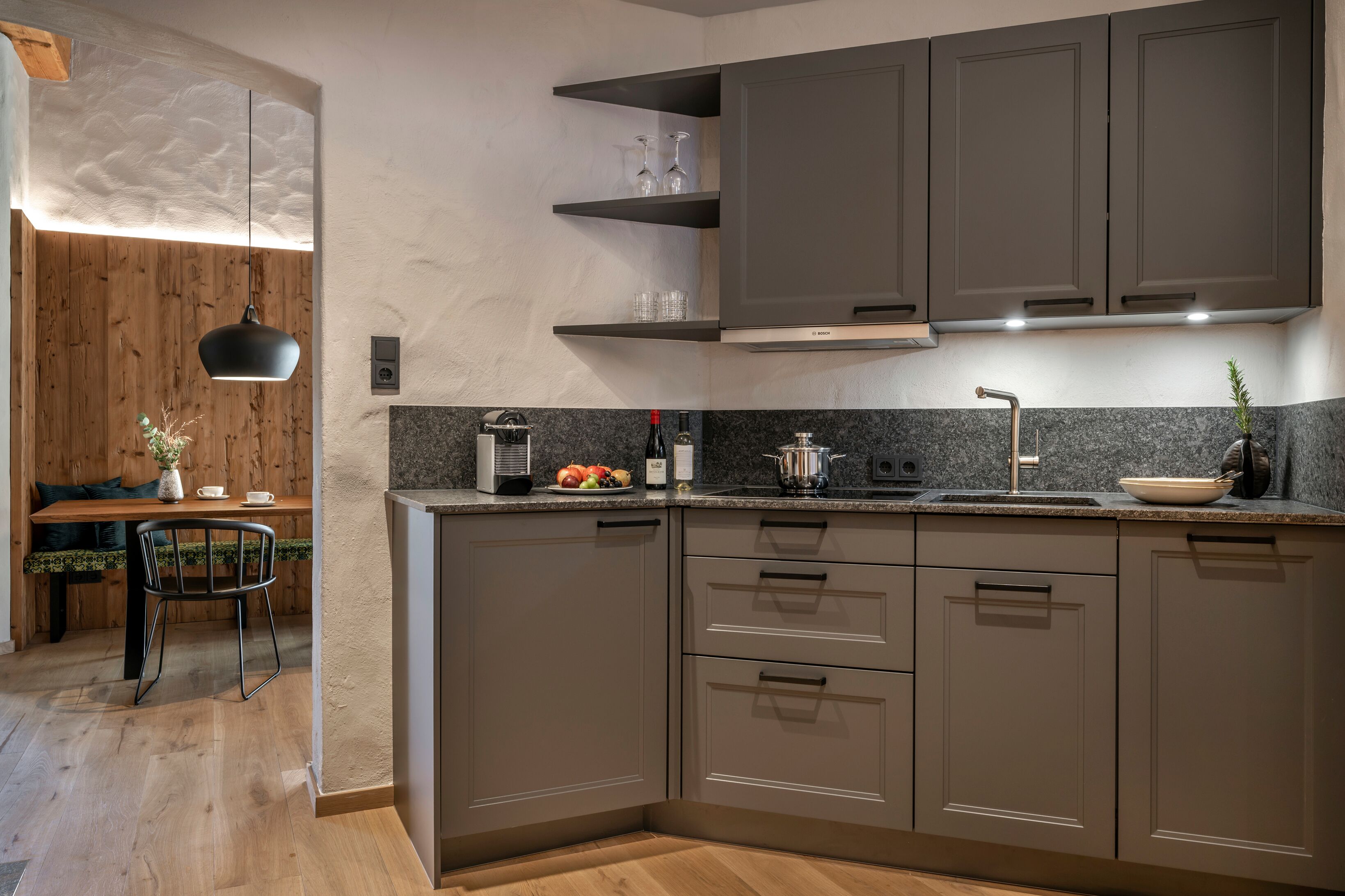 A modern kitchen with grey cabinets, a granite countertop, and a wooden dining area with a table and chairs.