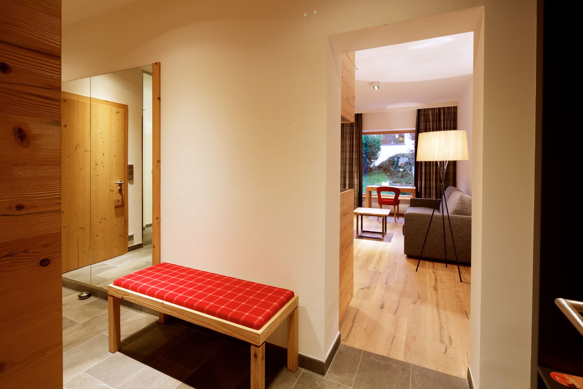 Ein Hotelzimmer mit einer Holzbank, einem kleinen Tisch, einer Couch und einer Lampe.