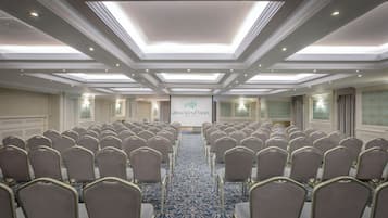 A conference room with rows of chairs, a carpeted floor, and a ceiling with recessed lighting.