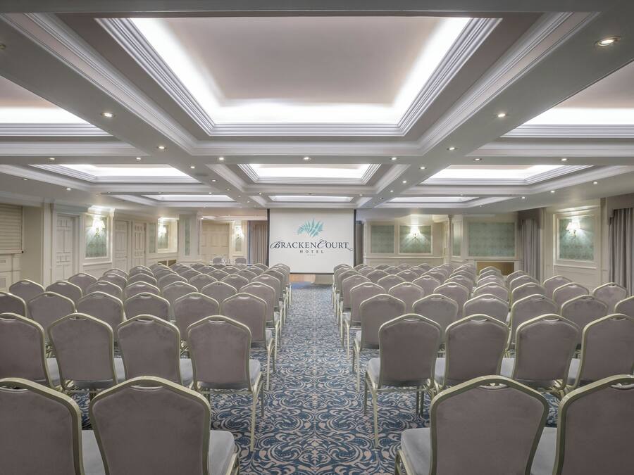 A conference room with rows of chairs, a carpeted floor, and a ceiling with recessed lighting.
