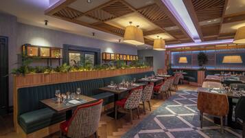 A restaurant with wooden ceiling beams, green upholstered booths, and tables set for dining.