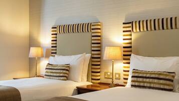 A hotel room with two beds, each with a striped pillow and a lamp.