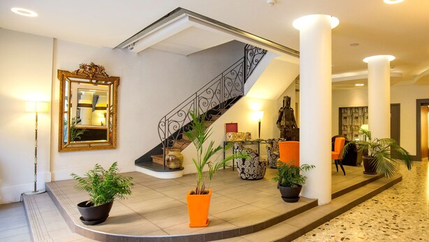 A spacious lobby with a curved staircase, potted plants, and a large mirror on the wall. - Hôtel Raymond 4 Toulouse (Toulouse)