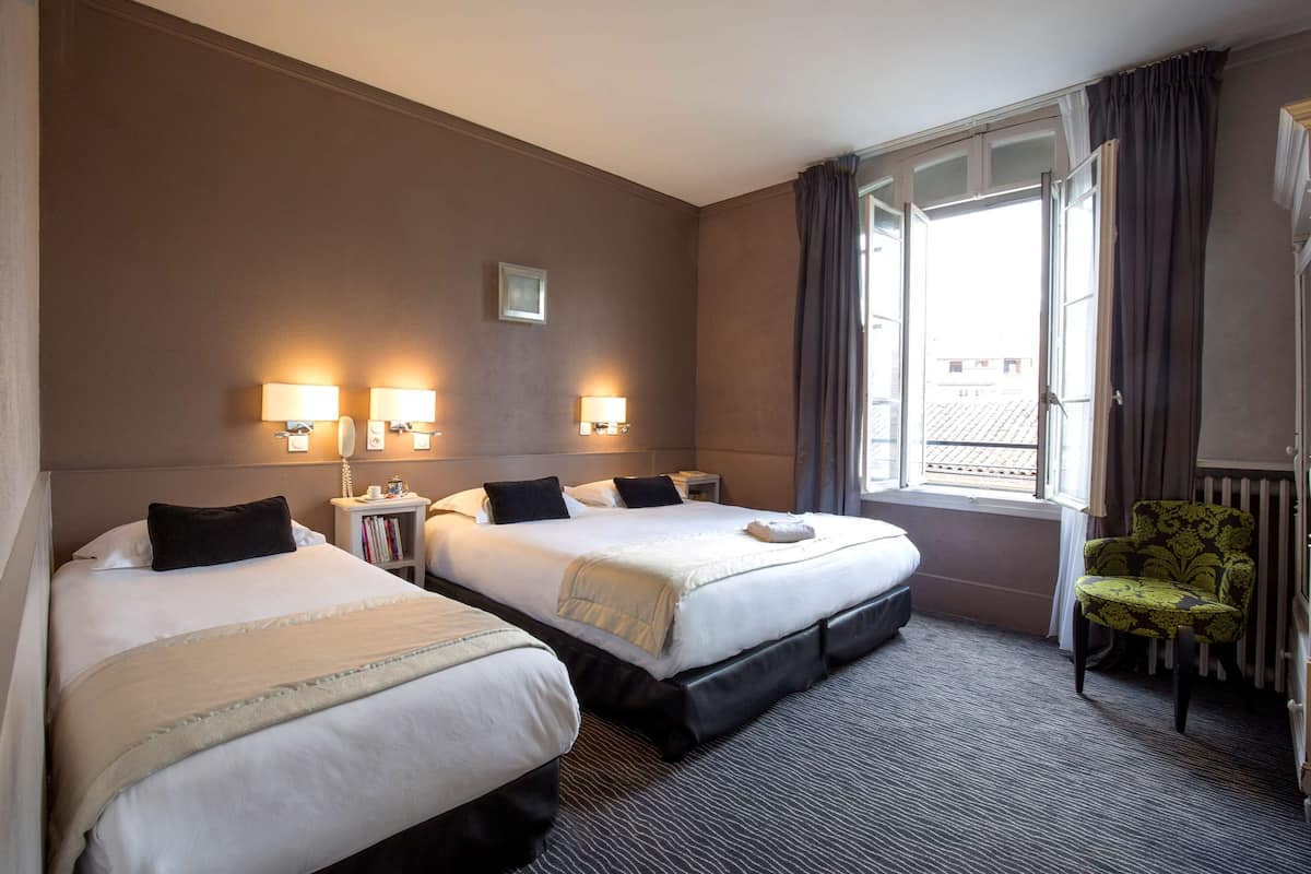 Een hotelkamer met twee bedden, nachtlampjes, een raam met gordijnen en een radiator.