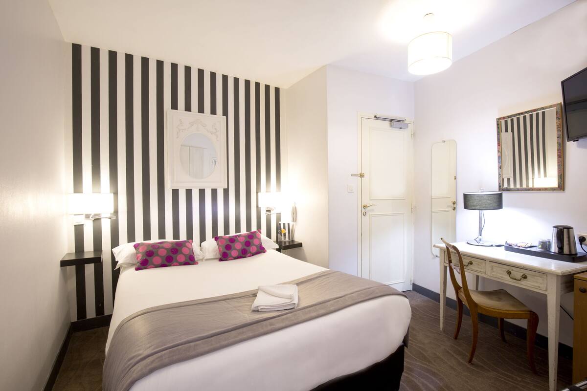 Een hotelkamer met een bed, nachtkastje, bureau, stoel en een spiegel.
