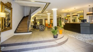 A hotel lobby with a staircase, seating area, reception desk, and decorative plants. - Hôtel Raymond 4 Toulouse (Toulouse)