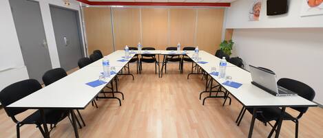 Una sala de conferencias con una larga mesa, sillas negras, botellas de agua y una computadora portátil.