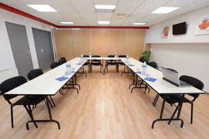 Una sala conferenze con un lungo tavolo, sedie nere, bottiglie d'acqua e un portatile.