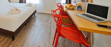 Habitación de hotel con cama, escritorio, una laptop, un bol de fruta y una botella de agua.