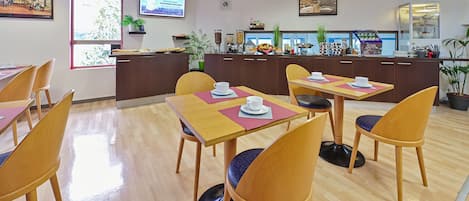 Un comedor de hotel con mesas y sillas de madera, una barra con estación de bebidas y una pantalla de televisión en la pared.