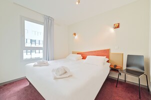 Una camera d'albergo con un letto grande, una sedia, un comodino e una finestra con tende.