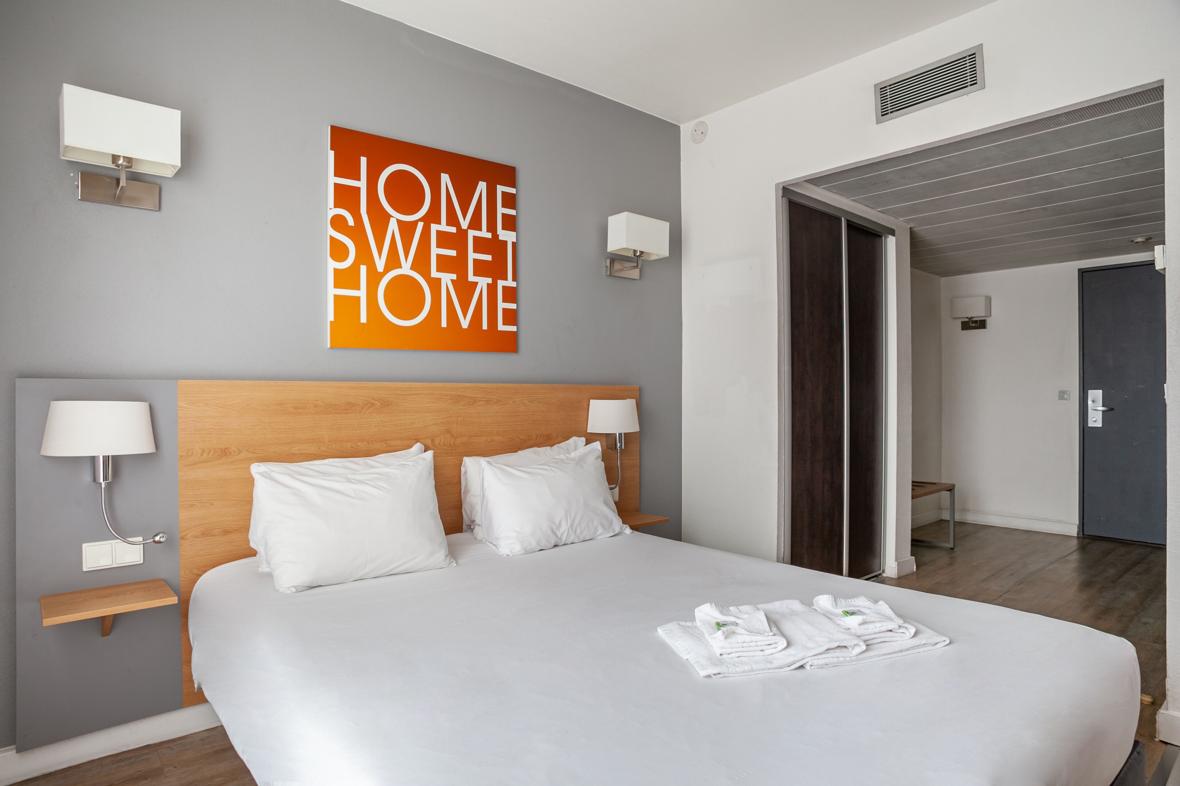 A hotel room with a large bed, two bedside tables with lamps, a wall-mounted artwork, and a door leading to another room.