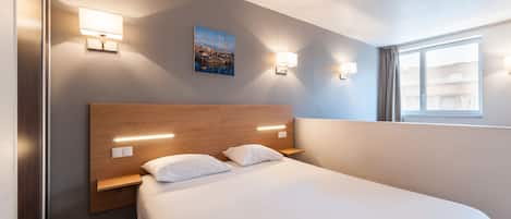 Hotelkamer met een groot bed, twee nachtkastjes, wandlampen, een schilderij en een raam met gordijnen.