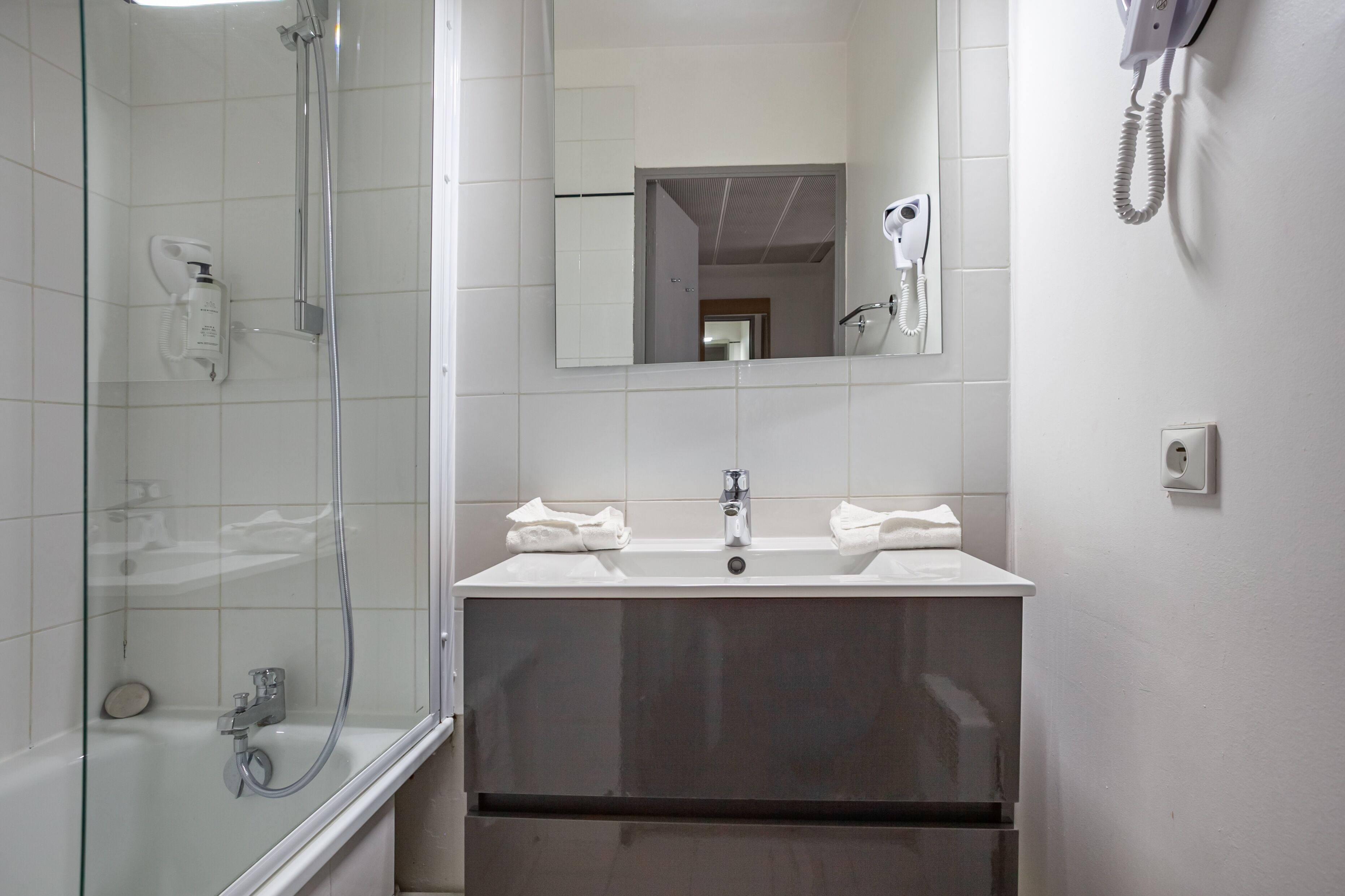 Un baño moderno con ducha de vidrio, un lavamanos con dos barras para toallas y un espejo sobre el lavamanos.