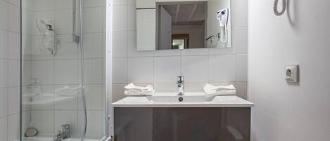 Un baño moderno con ducha de vidrio, un lavamanos con dos barras para toallas y un espejo sobre el lavamanos.
