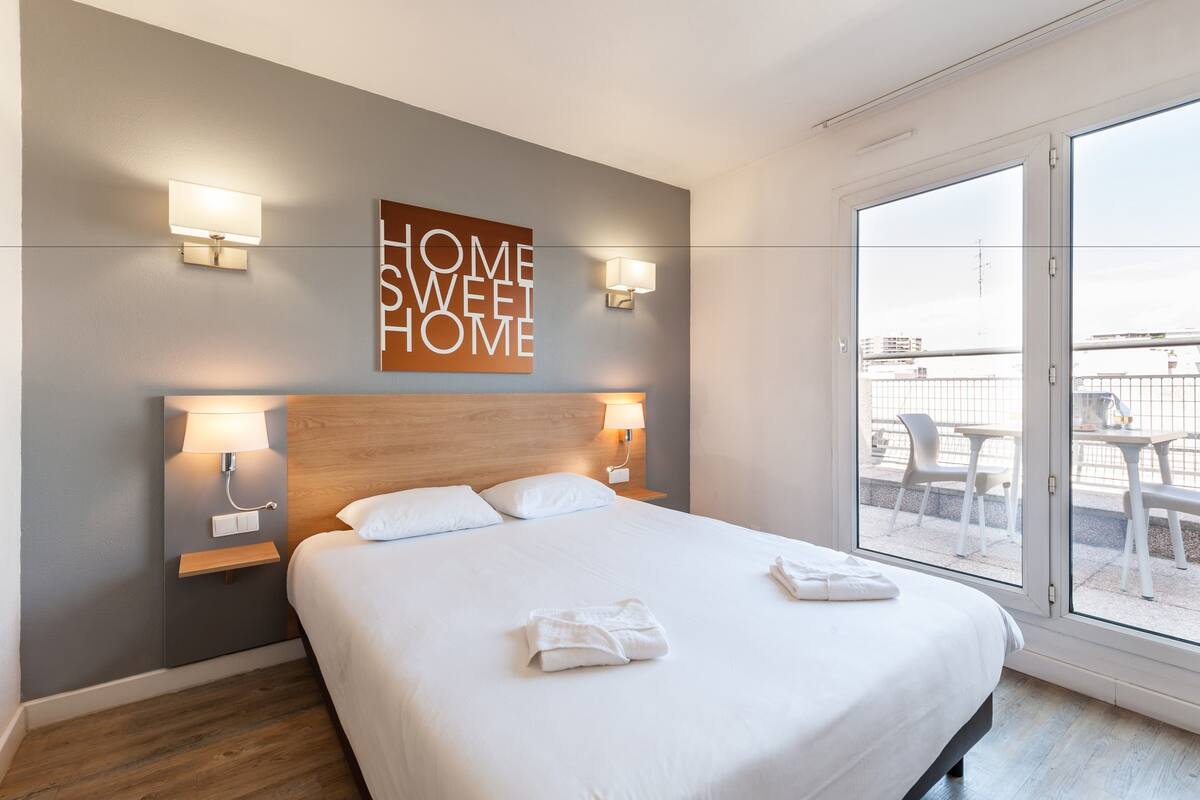 Ein ordentlich bezogenes Bett mit weißen Leinen und Handtüchern, ein hölzerner Kopfteil und ein an der Wand befestigtes Schild mit der Aufschrift 'HOME SWEET HOME'.