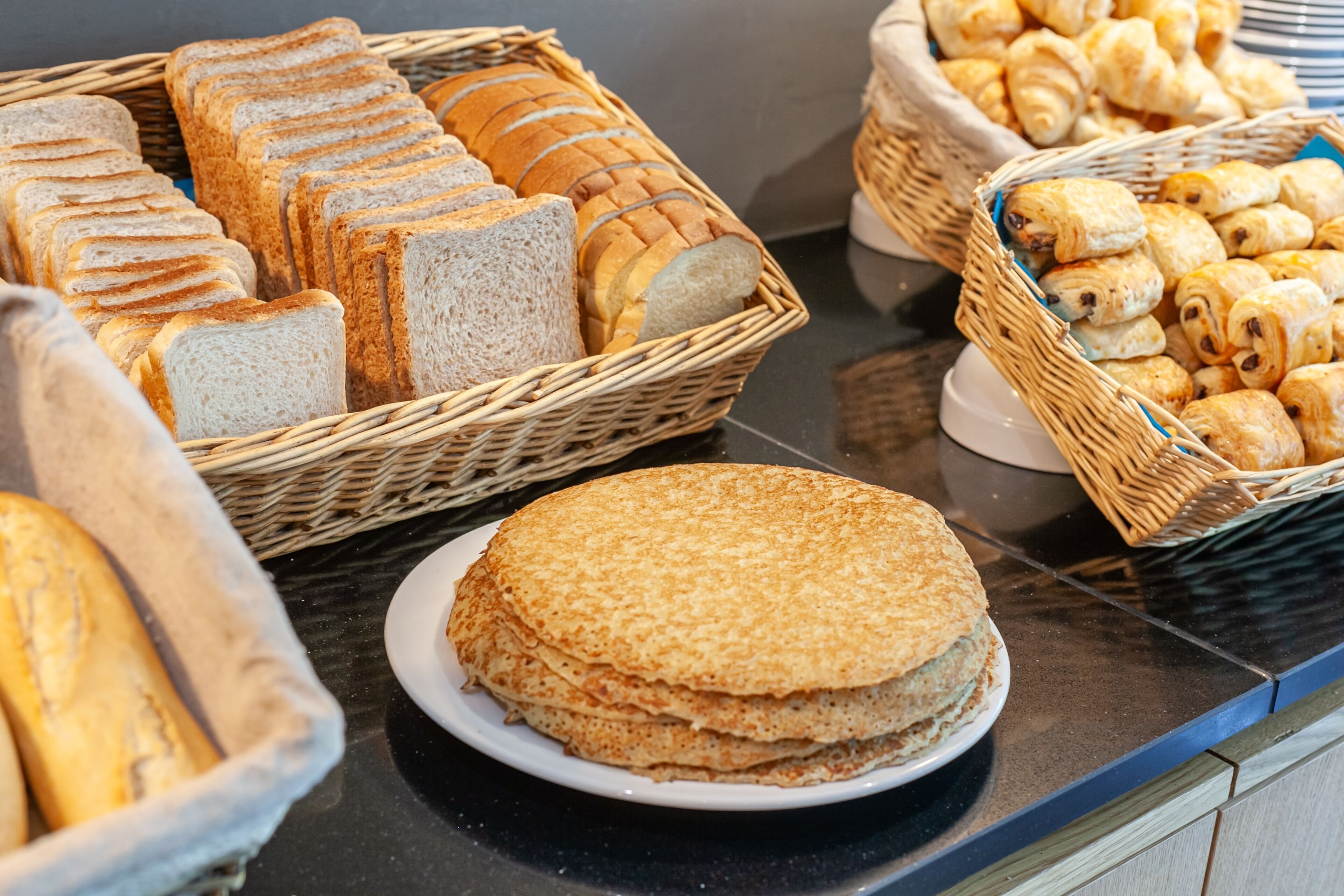 Un bufé con panes y pasteles diversos expuestos en cestas.