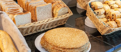 Un bufé con panes y pasteles diversos expuestos en cestas.