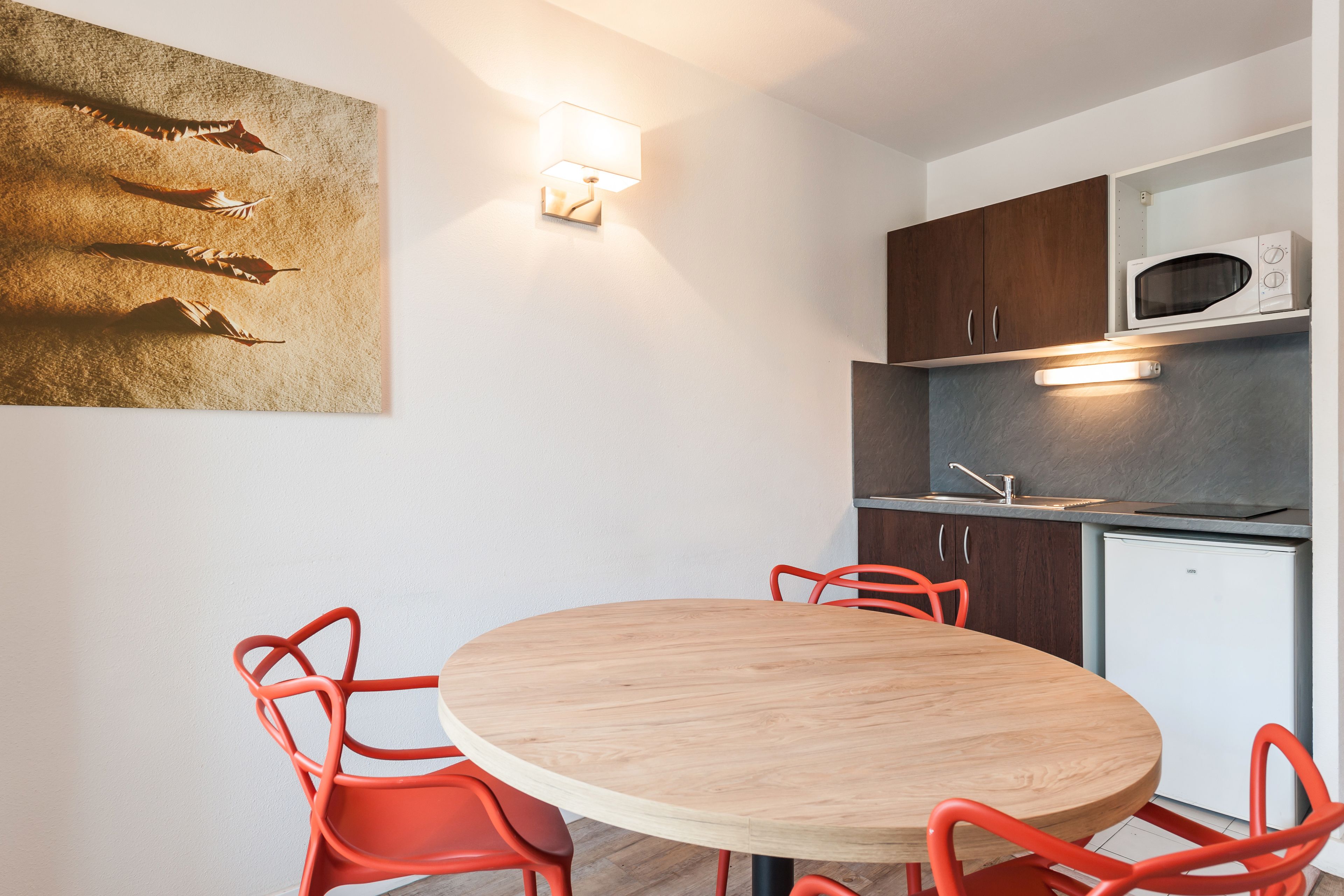 A modern kitchen with a round wooden table and red chairs, a microwave, and dark wooden cabinets.