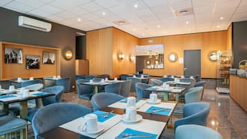 A modern hotel lobby with multiple dining tables, blue chairs, and a reception area.