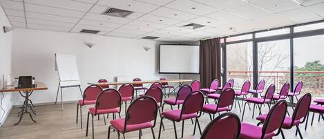 Un salón de conferencias con filas de sillas, una pantalla de proyector y una pizarra.