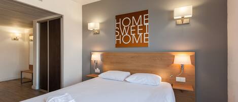 A hotel room with a large bed, two bedside tables with lamps, a wooden headboard, and a wall-mounted sign that reads "HOME SWEET HOME".