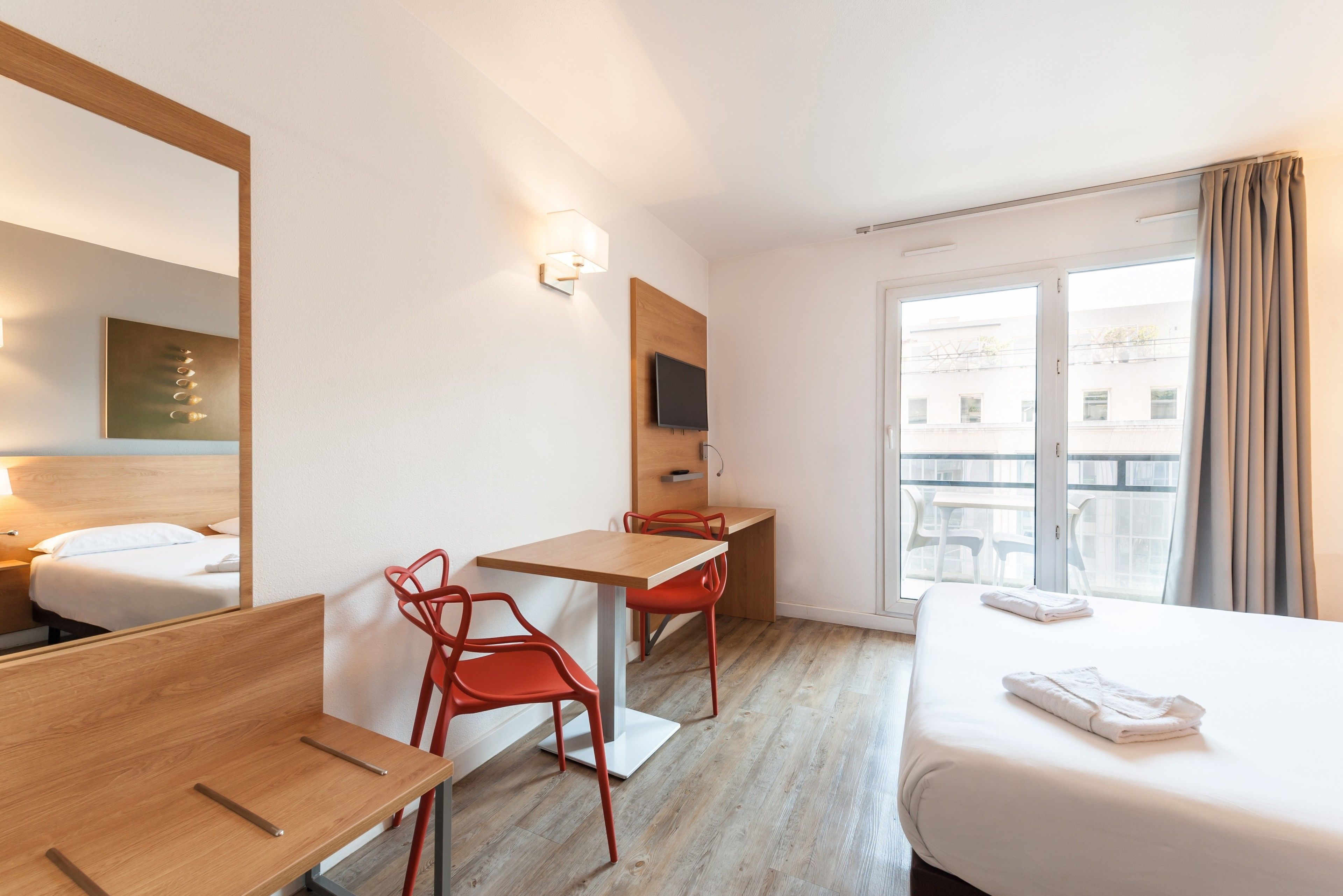 Habitación de hotel con cama, escritorio, dos sillas, televisor y ventana con cortinas.