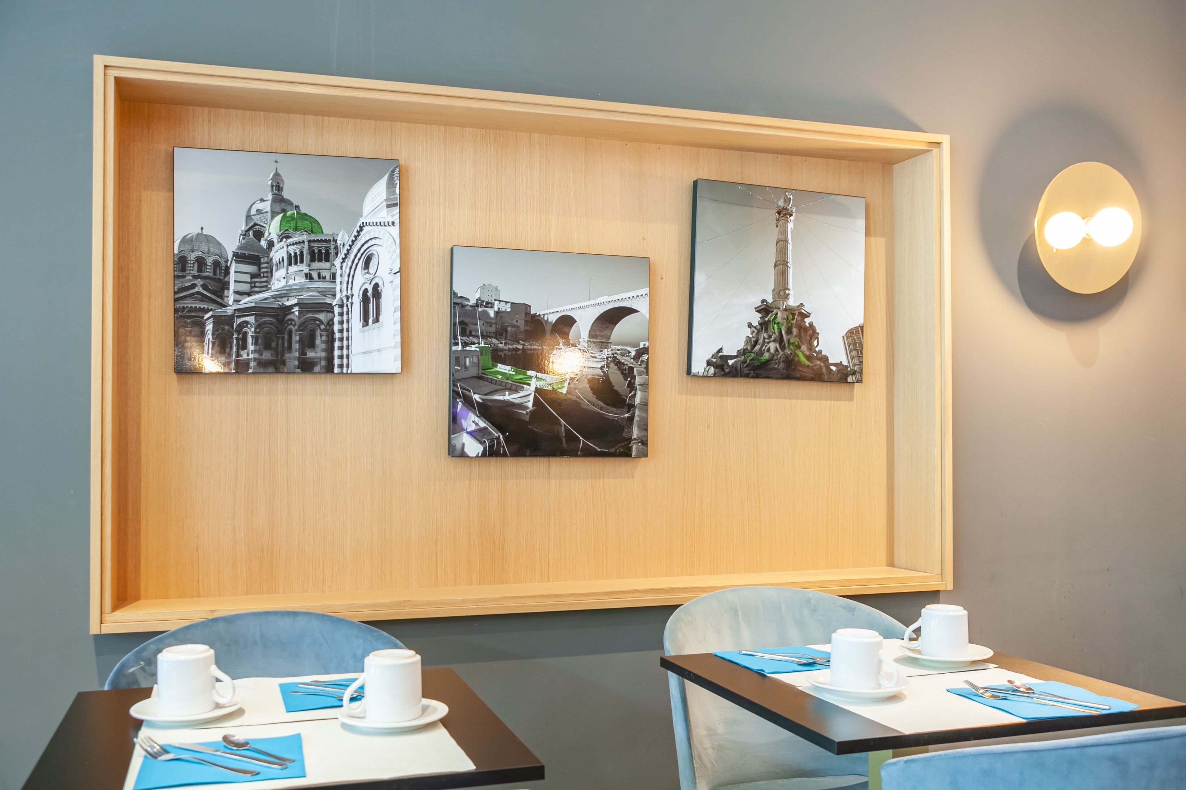 A hotel lobby with three framed pictures on the wall, two tables with chairs, and a wall-mounted light fixture.