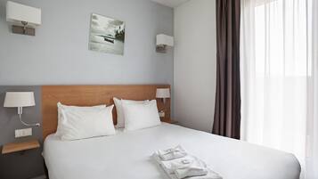 Una habitació d'hotel amb un llit gran, dues taules de nit amb làmpades, un quadre a la paret i una finestra amb cortines.