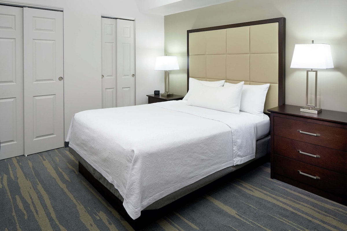 A hotel room with a bed, nightstands, a dresser, and a door.