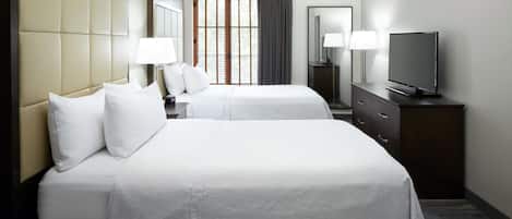 A hotel room with two beds, a TV, a dresser, and a window with curtains.