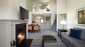 A modern living room with a fireplace, a sofa, a flat-screen TV, and a staircase leading to an upper level.