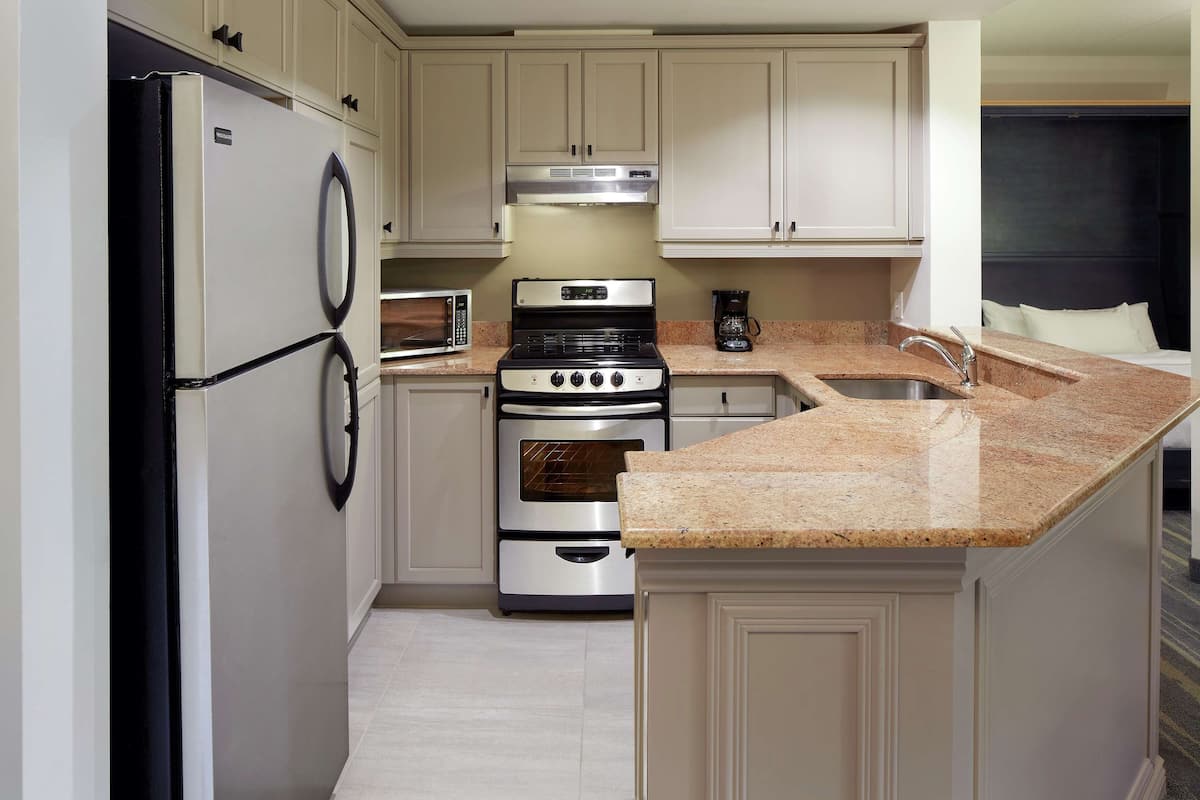 A compact kitchen with a refrigerator, microwave, stove, oven, and granite countertop.
