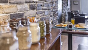 A breakfast table with jars of condiments, a glass of orange juice, and plates of food.