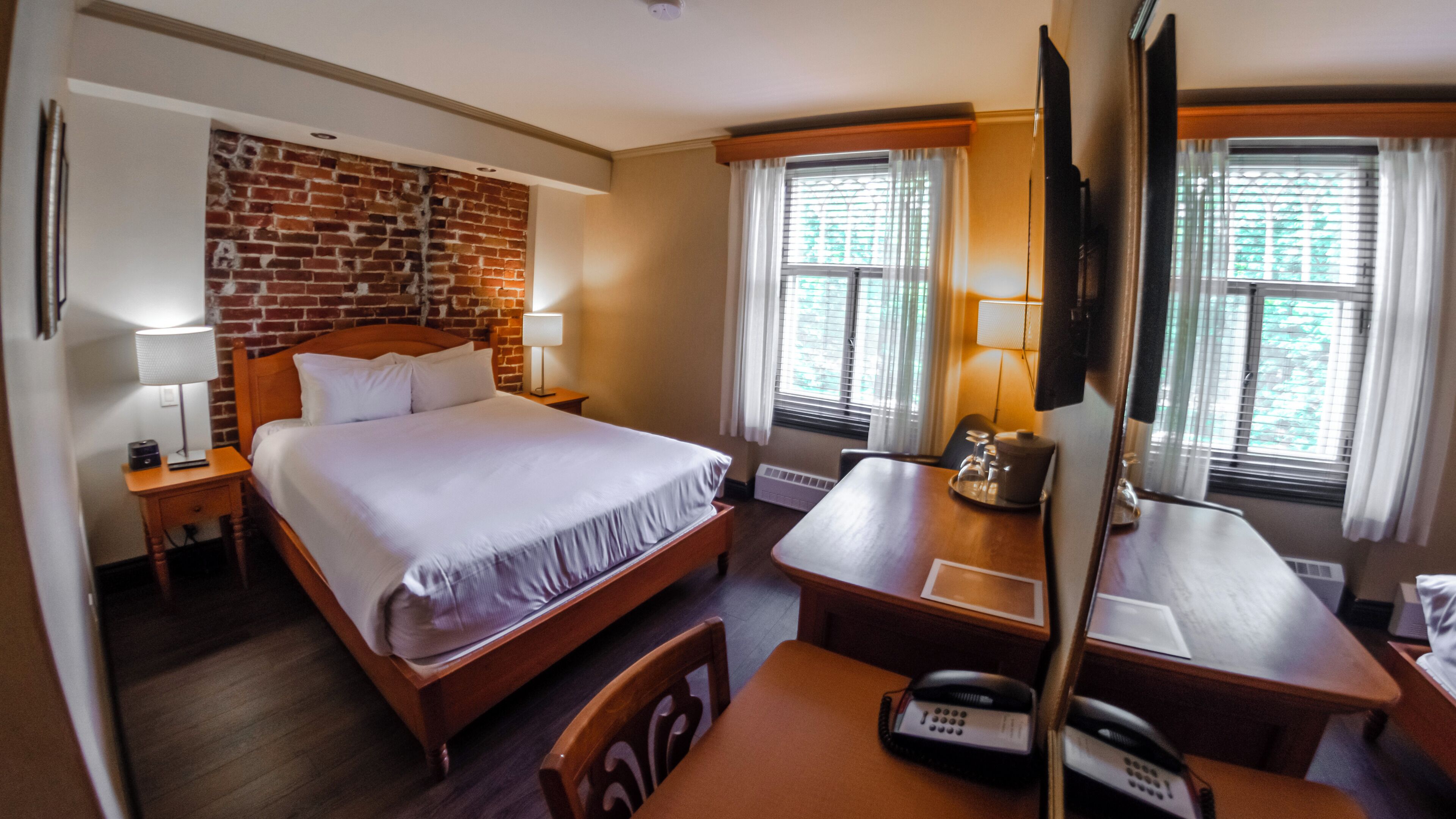 Habitación de hotel con pared de ladrillo decorativa, una cama grande, un escritorio con teléfono y una silla.