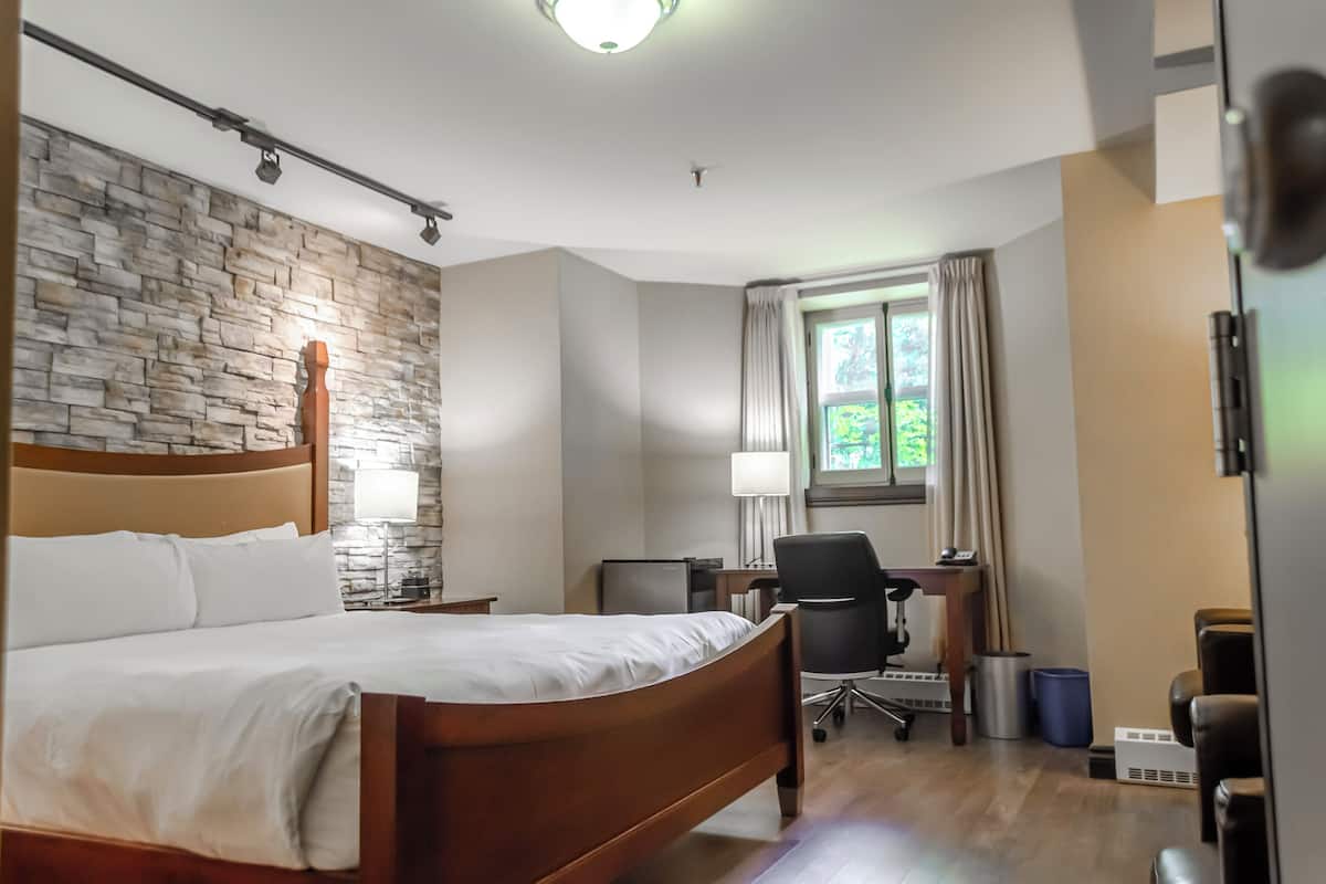 Habitación de hotel con cama de madera, un escritorio con silla, una lámpara y vista a zonas verdes.